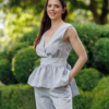 A dark-haired woman wearing an elegant blue melange top, with a belt at the waist, a V-neckline and an open back, and blue melange pants, made of 100% linen.