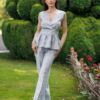 A dark-haired woman wearing an elegant blue melange top, with a belt at the waist, a V-neckline and an open back, and blue melange pants, made of 100% linen.