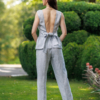 A dark-haired woman wearing an elegant blue melange top, with a belt at the waist, a V-neckline and an open back, and blue melange pants, made of 100% linen.