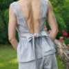 A dark-haired woman wearing an elegant blue melange top, with a belt at the waist, a V-neckline and an open back, and blue melange pants, made of 100% linen.