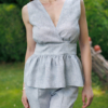A dark-haired woman wearing an elegant blue melange top, with a belt at the waist, a V-neckline and an open back, and blue melange pants, made of 100% linen.