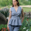 A dark-haired woman wearing an elegant blue striped top, with a belt at the waist, a V-neckline and an open back, and dark blue pants made of 100% linen.
