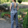 A dark-haired woman wearing an elegant blue striped top, with a belt at the waist, a V-neckline and an open back, and dark blue pants made of 100% linen.