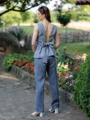 A dark-haired woman wearing an elegant blue striped top, with a belt at the waist, a V-neckline and an open back, and dark blue pants made of 100% linen.