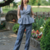 A dark-haired woman wearing an elegant blue striped top, with a belt at the waist, a V-neckline and an open back, and dark blue pants made of 100% linen.