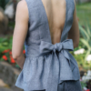 A dark-haired woman wearing an elegant blue striped top, with a belt at the waist, a V-neckline and an open back, and dark blue pants made of 100% linen.