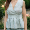 A dark-haired woman wearing an elegant green striped top, with a belt at the waist, a V-neckline and an open back, made of 100% linen.