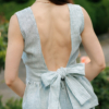 A dark-haired woman wearing an elegant green striped top, with a belt at the waist, a V-neckline and an open back, made of 100% linen.