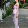 A dark-haired woman wearing a pink elegant top with a belt at the waist, a V-neckline and an open back, and pink pants made of 100% linen.