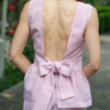 A dark-haired woman wearing a pink elegant top with a belt at the waist, a V-neckline and an open back, and pink pants made of 100% linen.