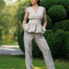 A dark-haired woman wearing a beige elegant top with a belt at the waist, a V-neckline and an open back, and beige pants made of 100% linen.