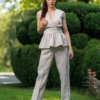 A dark-haired woman wearing a beige elegant top with a belt at the waist, a V-neckline and an open back, and beige pants made of 100% linen.