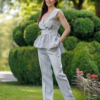 A dark-haired woman wearing an elegant blue melange top, with a belt at the waist, a V-neckline and an open back, and blue melange pants, made of 100% linen.