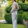 A dark-haired woman wearing an elegant blue melange top, with a belt at the waist, a V-neckline and an open back, and blue melange pants, made of 100% linen.