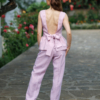 A dark-haired woman wearing a pink elegant top with a belt at the waist, a V-neckline and an open back, and pink pants made of 100% linen.