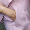 A dark-haired woman wearing a pink elegant top with a belt at the waist, a V-neckline and an open back, and pink pants made of 100% linen.